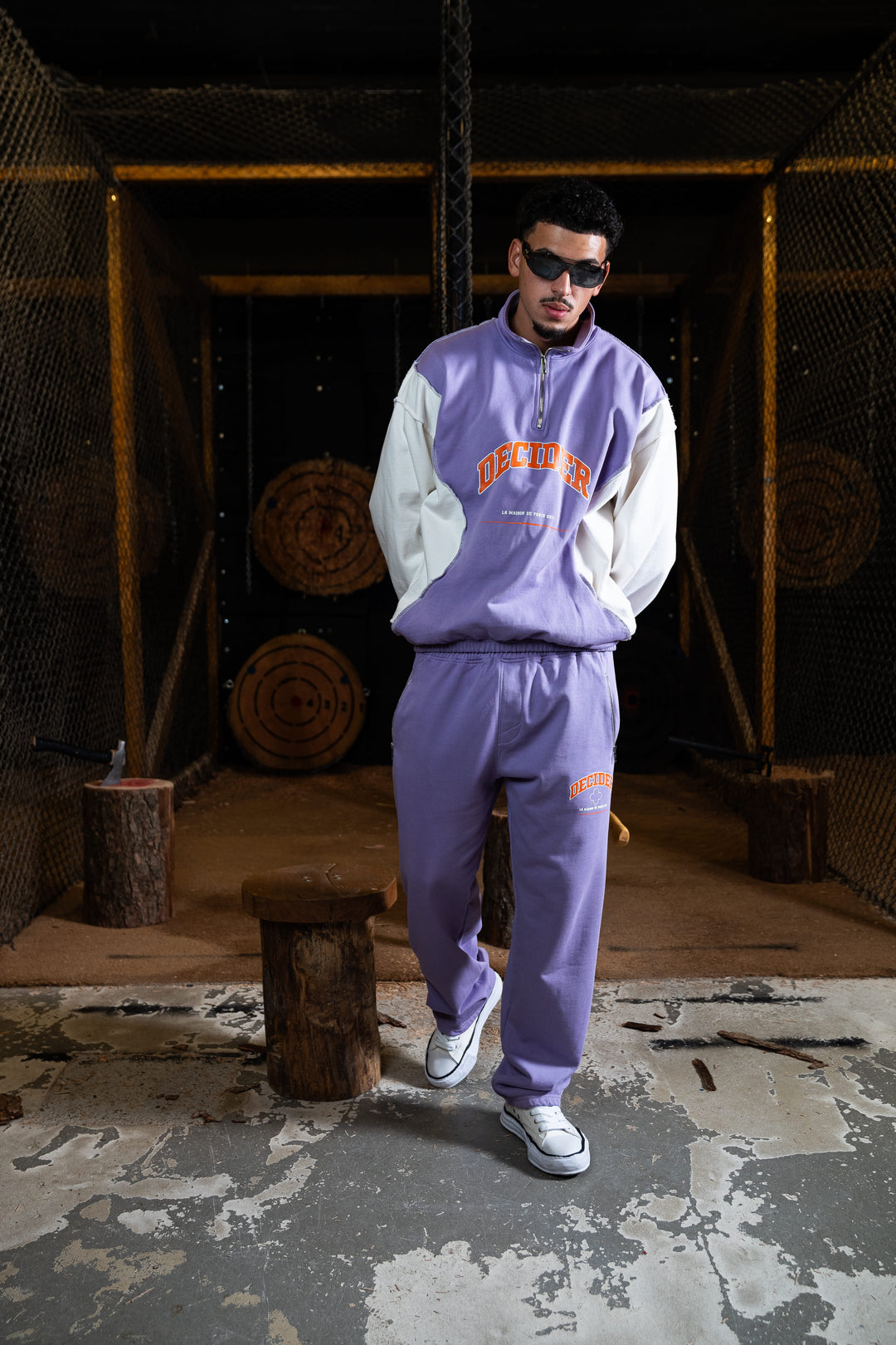Männliches Model posiert in einer rustikalen Umgebung, gekleidet in Deciders Sweatpants und Pullover in Pastel-Lila