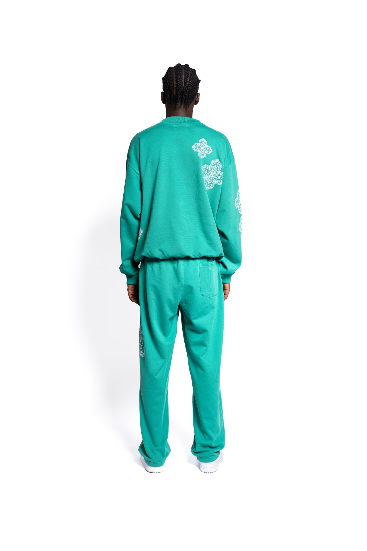 Rückansicht eines Modells in smaragdgrünen Sweatpants und passendem Sweat Shirt. Die Hosen verfügen über Taschen und ein feines, diamantähnliches Muster entlang der Seitennaht, das eine elegante Note in das Streetwear Outfit bringt.